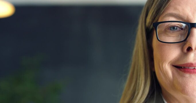 Close up of half face of senior Caucasian beautiful wise woman in glasses smiling slight to camera indoor. Portrait of businesswoman looking straight.