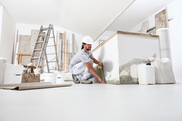 construction worker plasterer man measuring wall with measure tape in building site of home...