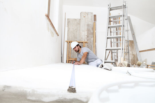 construction worker plasterer man measuring wall with measure tape in building site of home renovation with tools and building materials on the floor