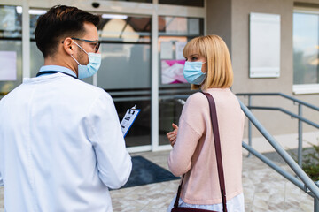 Obraz premium Young male practitioner or doctor talking with female patient or visitor in front of hospital entrance. Healthcare concept.