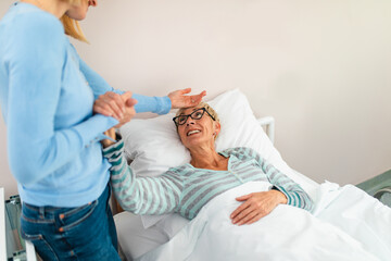 Beautiful middle age woman spending some time with her mother in hospital or nursing center. Senior woman lying in bed.