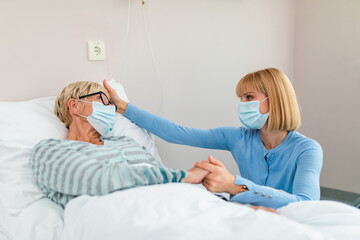 Beautiful middle age woman spending some time with her mother in hospital or nursing center. Senior woman lying in bed.