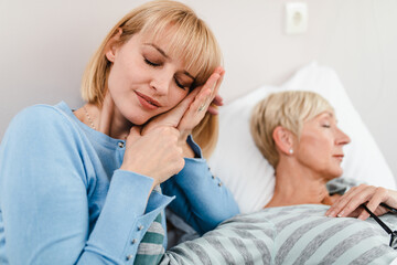 Beautiful middle age woman spending some time with her mother in hospital or nursing center. Senior woman lying in bed.