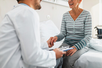 Obraz premium Young doctor visiting sick senior woman in hospital room or nursing center.