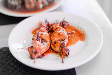Grilled Squids on wooden sticks on white plate in spicy sause. A dish of Chinese cuisine.