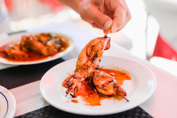 Grilled Squids on wooden sticks on white plate in spicy sause. A dish of Chinese cuisine.