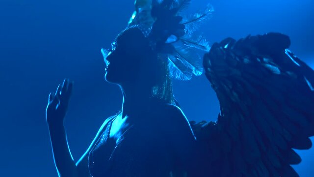 Silhouette of a dancing woman with wings on her back. Greek goddess Artemis in a theatrical vocal dance show with blue neon lights. Close up.