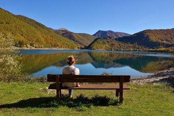 Woman relaxing on a bench in front of lake and mountain