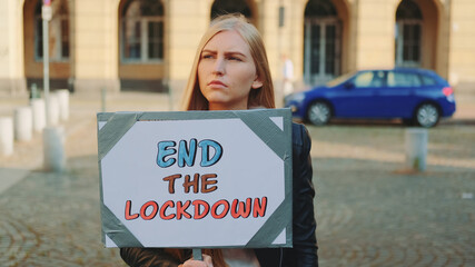 Young woman asking to end lockdown on protest march by walking on the street with banner.
