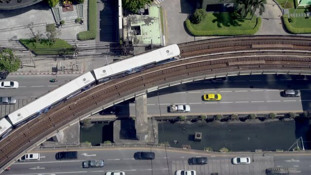 top view of rail skytrain with transport mass transit train move on rail bridge over car and vehicle drive on local road in business city. 