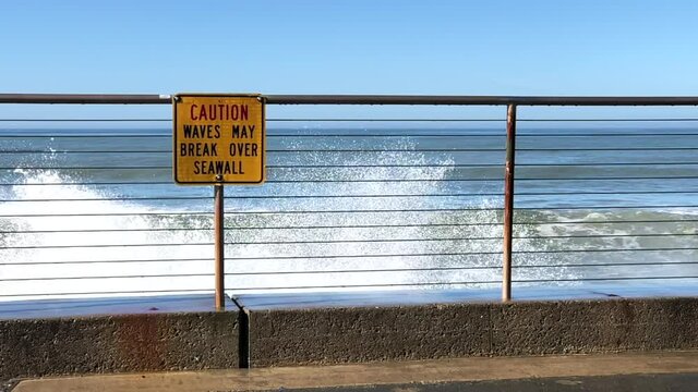 HD video slow motion of Sea Wall with caution sign about waves breaking over it, slow motion of a wave breaking and spraying up over the sea wall.

