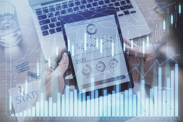 Double exposure of man's hands holding and using a digital device and forex graph drawing. Financial market concept.