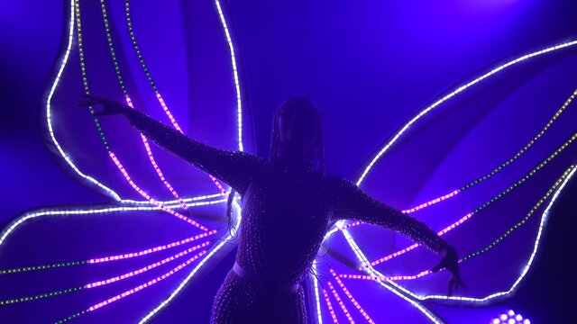 Actress as a Butterfly with flashing glowing wings. Woman singing and dancing in the studio with purple neon lights. Close up.