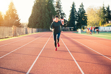 Fototapeta premium Asian woman running on the track in the winter. Sun flare suggests sunrise or sunset.