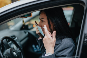 Attractive middle age business woman with protective face mask driving her car. She is confident and positive. Coronavirus or Covid-19 pandemic lifestyle concept.