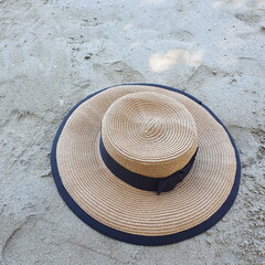 Fototapeta na wymiar A vintage style wide brim hat with a black ribbon and a bow attached to the hat rests on the beach rocks. Always wear a hat to protect against UV rays from the sun while outdoors or in fashionable hat
