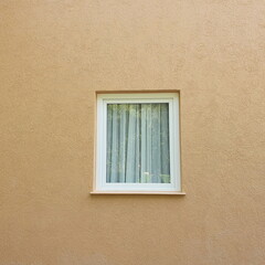 Vintage-style glass-paneled windows with thin curtains White aluminum frame and fixed frame on light brown concrete wall. Modern windows with nature in plaster walls.
