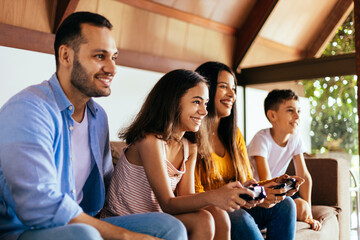 Latin family enjoying the day together at home playing video games on the couch