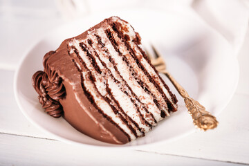 A piece of chocolate cake on a white plate with a gold fork on a white plate. Traditional sweets for birthday and other holidays