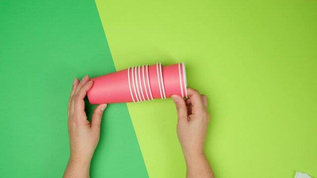 two female hands holding a stack of red paper cups on a green background, rejection of plastic, zero waste
