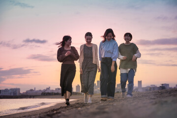 夕暮れの中、寄り添って海沿いを歩く女性4人