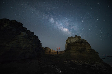 Milky Way by the sea at night, with a man standing on the edge of a huge reef, Zhangzhou Volcano Geological Park, Xiamen, Fujian