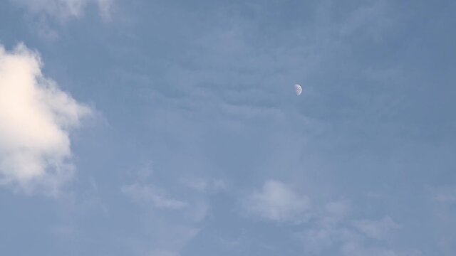 Moon in its first quarter time lapse as seen before dark with clouds almost covering it on the right side of the frame.