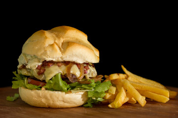 Close up of a homemade burger with bacon and salad a chopping wood board, on black background