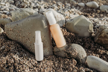 Cosmetic serum bottles on natural stone on the beach . sea natural background, concept of natural skin care products. Skincare essence for beautiful healthy skin. sunscreen lotion.