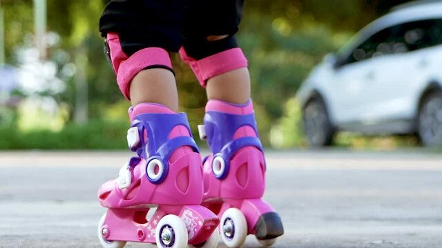 Little girl wearing protection pads and safety helmet learning to roller skate in summer park. Active outdoor sport for kids. Close-up legs