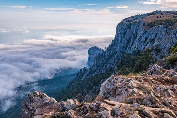 A majestic view of the rocky mountains and the valley in fog and clouds. Creamy fog covered the mountain valley in sunset light. Picturesque and gorgeous scene. Misty sunset over Crimea Mountains