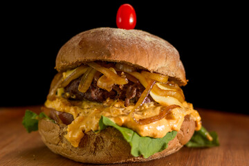 Close up of a homemade burger with onions and cheddar on a chopping wood board, on black background