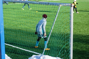 Boys in gray yellow sportswear running on soccer field with snow on background. Young footballers dribble and kick football ball in game. Training, active lifestyle, sport, children winter activity