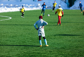 Boys in gray yellow sportswear running on soccer field with snow on background. Young footballers dribble and kick football ball in game. Training, active lifestyle, sport, children winter activity