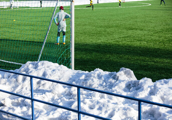 Boys in gray yellow sportswear running on soccer field with snow on background. Young footballers dribble and kick football ball in game. Training, active lifestyle, sport, children winter activity