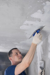 master in protective gloves for repairing concrete walls, aligns the ceiling with a spatula