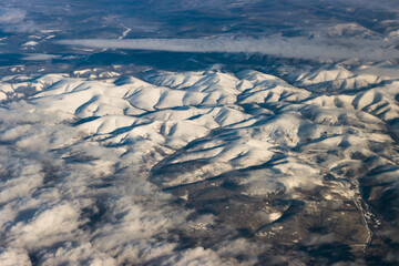 Snowy mountains from a bird's eye view on a clear blue sky with clouds.