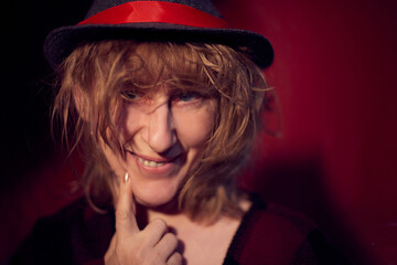 Portrait of fun middle-aged woman with smile in hat on red background. Female model posing in the Studio.