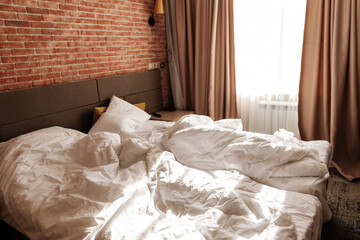 Fototapeta na wymiar Unmade two beds with white blankets and pillows at window. Loft apartment with red brick wall. Minimalist or scandinavian style of interior design. Spacious bedroom with furniture