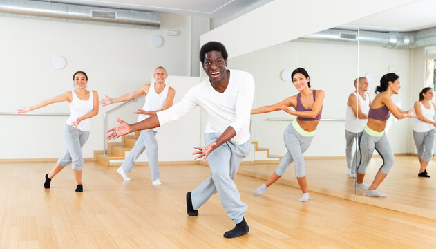 Portrait of emotional young adult man doing exercises during group class in dance center