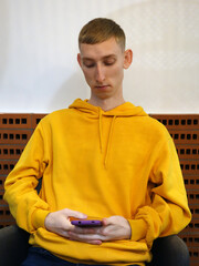 Portrait of handsome guy wearing casual yellow hoodie and using phone.