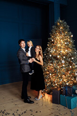 Happy parents with preschool son stand near Christmas tree, caring dad hold overjoyed child in arms, loving mom hug cute kid, celebrate new year at home, winter holidays concept