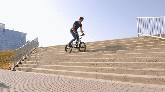 A young guy does stunts on a BMX bike in the Park on the stairs, he jumps from step to step.