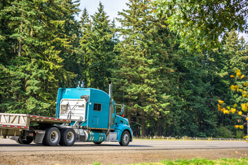 Bright blue big rig semi truck with aluminum step down semi trailer driving on the green highway