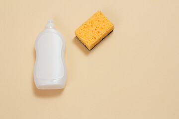 Bottle of dishwashing liquid and sponge on a beige background.