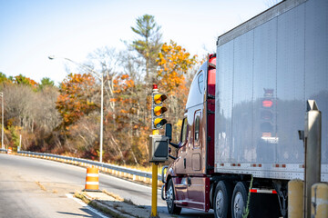 Red big rig shiny semi truck with dry van semi trailer standing on the highway entrance with traffic light