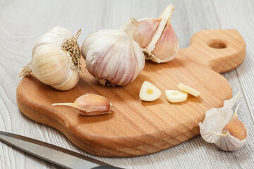 Ripe garlic heads and stainless steel knife on wooden cutting board