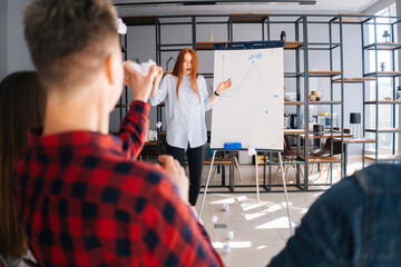 Redhead young business woman finishing report on white board. Dissatisfied colleagues throw crumpled paper balls at frightened lady. Confused female runs away and hides behind blackboard.