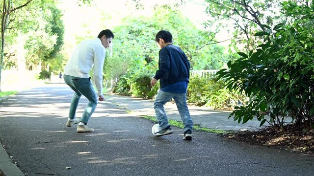 サッカーボールを蹴る息子のサポートをするお父さん
