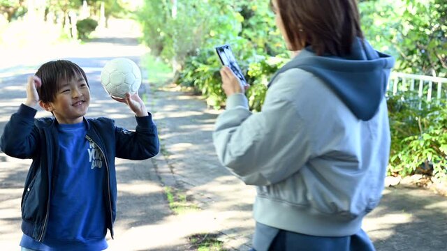 ボールを掲げてポーズをとる息子の写真を、スマートフォンで撮るお母さん